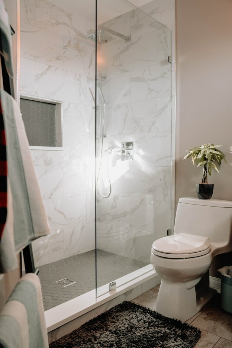 Moderne badkamer met glazen douche, witte marmeren tegels, toilet en een klein plantje op het reservoir.