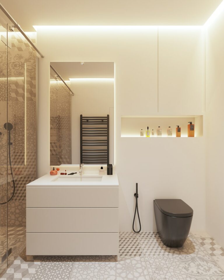 Moderne badkamer met een witte wastafel, grote spiegel en zwart toilet. Douchegedeelte heeft een glazen deur. Toiletartikelen staan op een verzonken plank boven het toilet. Gepatroneerde vloertegels maken het decor compleet.