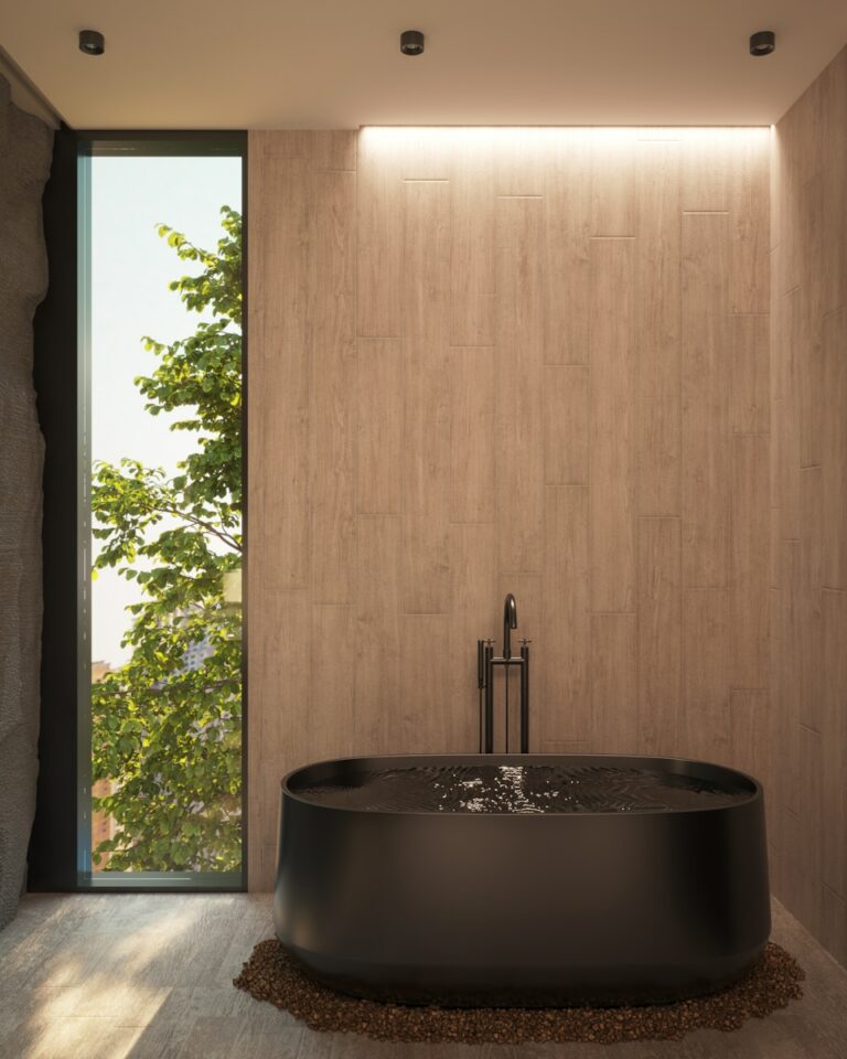 Moderne badkamer met een zwart vrijstaand bad op een kiezelstenen basis, een groot verticaal raam met groen en houten paneelwanden. Plafondverlichting verlicht de ruimte zachtjes.