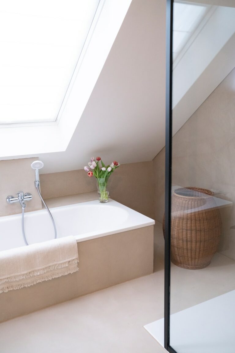 Moderne badkamer met beige bad, tulpenvaas, dakraam en rieten mand.