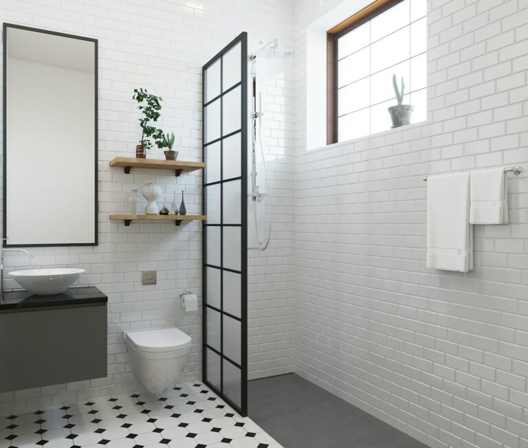 Minimalistische badkamer met witte betegelde muren en zwarte accenten, voorzien van een zwarte glazen douchewand, een hangend toilet, een wastafel, decoratieve planken en een raam met een cactus.