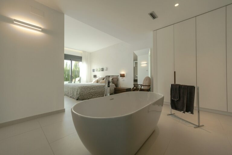 Moderne slaapkamer met een open indeling, voorzien van een vrijstaand bad, een groot bed, een kast en natuurlijk licht via een raam.